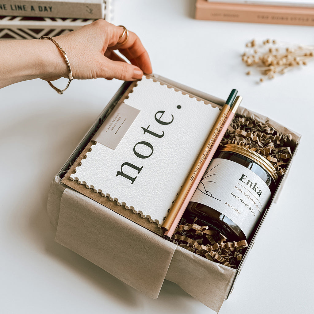 The byFoke Kaisa Notecard and candle gift set, open on a table containing Katie Leamon Notecard Set, 2 pencils and a byFoke essential oil soy wax candle.