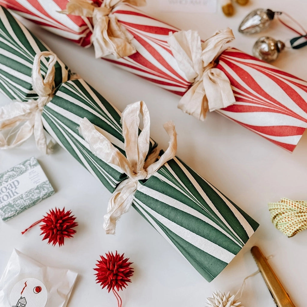 One Candy Cane Green Christmas Cracker and one Candy Cane Red Christmas Cracker surrounded by little gifts  and Christmas decorations to put in the crackers.