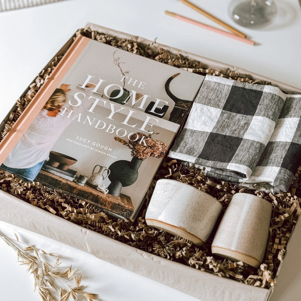 A byFoke gift box containing "The Home Style Handbook" by Lucy Gough, two folded black and white gingham napkins, a handmade ceramic jug and coffee bowl. The presentation is stylish and elegant.