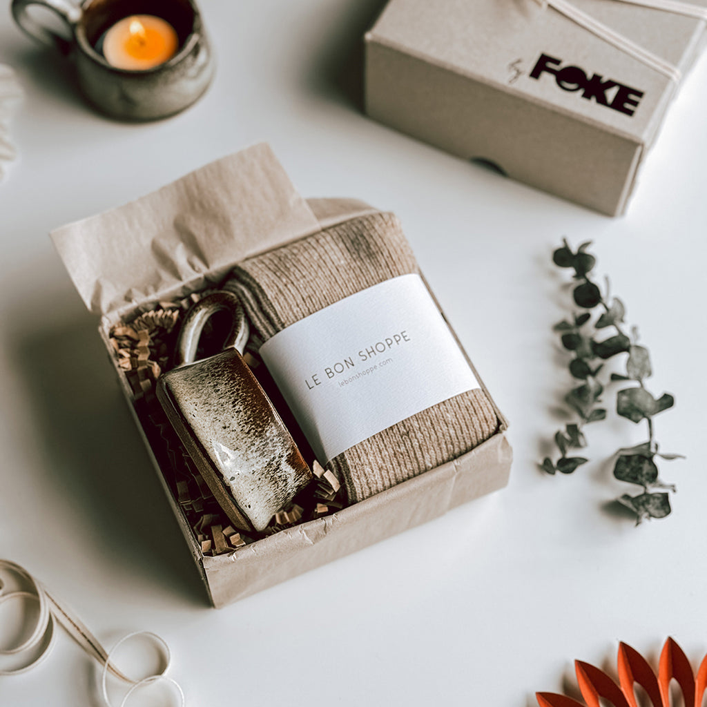 An open byFoke Gift Box with a pair of Le Bon Shoppe Snow Socks in Tan and a stoneware candle holder.