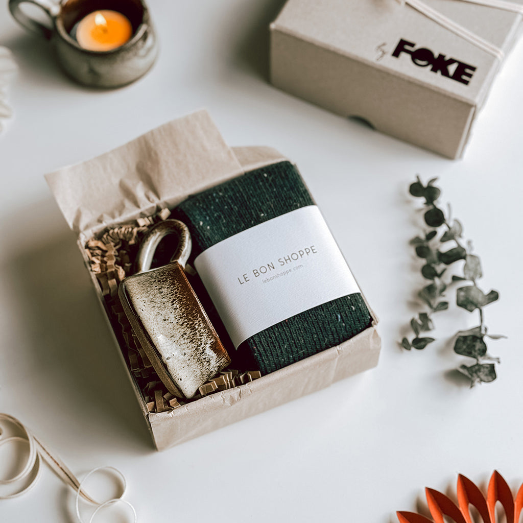 An open byFoke Gift Box with a pair of Le Bon Shoppe Snow Socks in Forest and a stoneware candle holder.