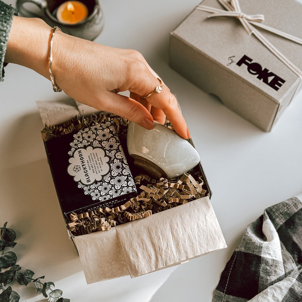 An open byFoke Gift Box containing a mini cream bowl and a box of Blackthorn Sea Salt. A hand is lifting the bowl up out of the box.