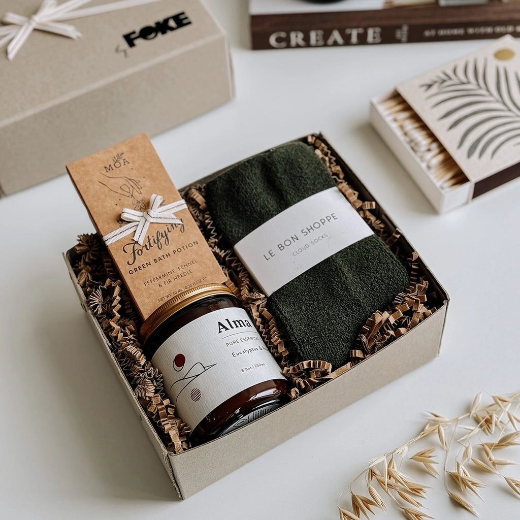 The Perdy Gift Box byFoke laying open on a table. The gift box contains; Cloud Socks by Le Bon Shoppe in Forest, Alma Essential Oil Soy Wax Candle, Fortifying Green Bath Potion by MOA.
