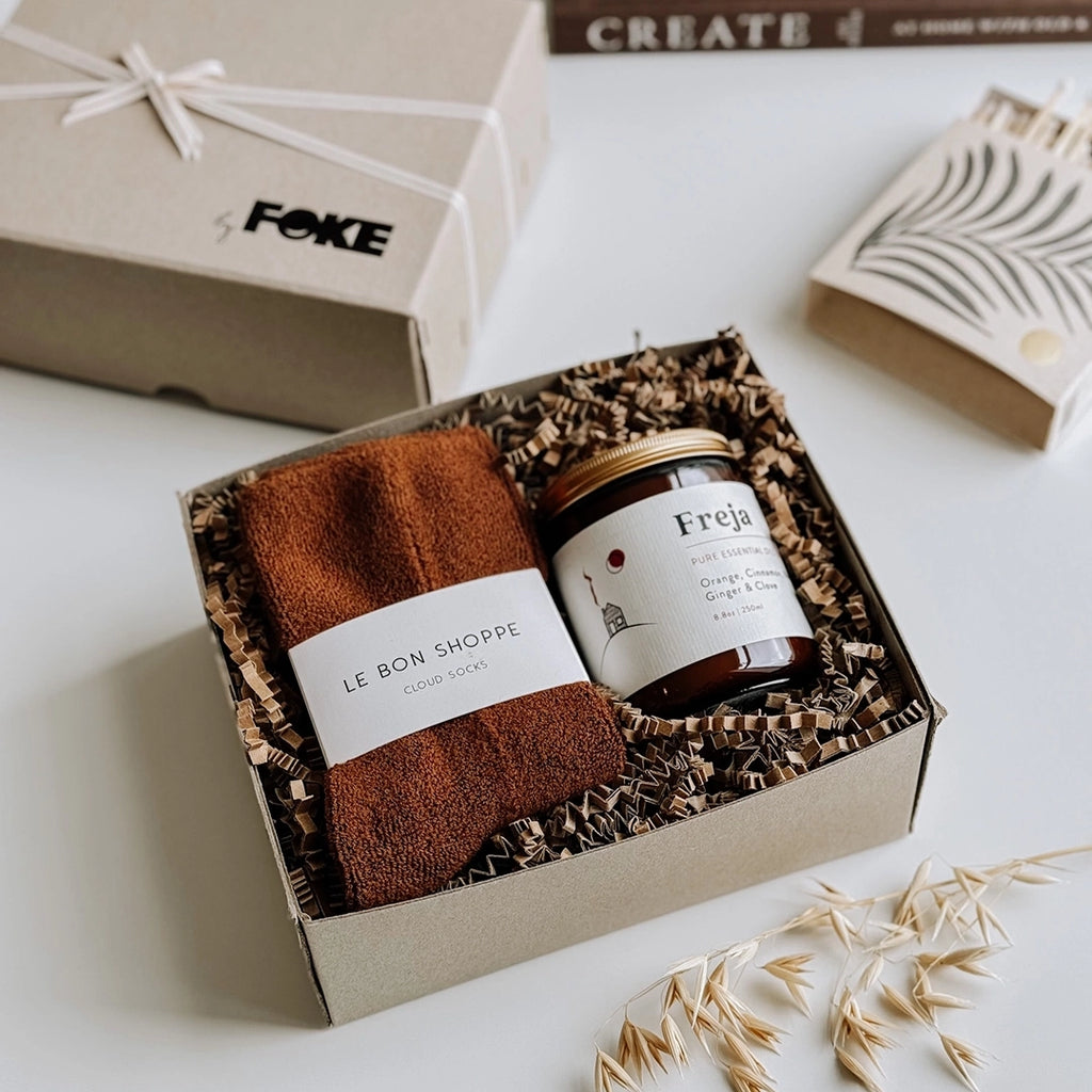 A beautiful photo of byFoke's Chloe Gift Box, opened with the lid to one side. Inside the gift box is a pair of sepia cloud socks and a Freja essential oil candle.