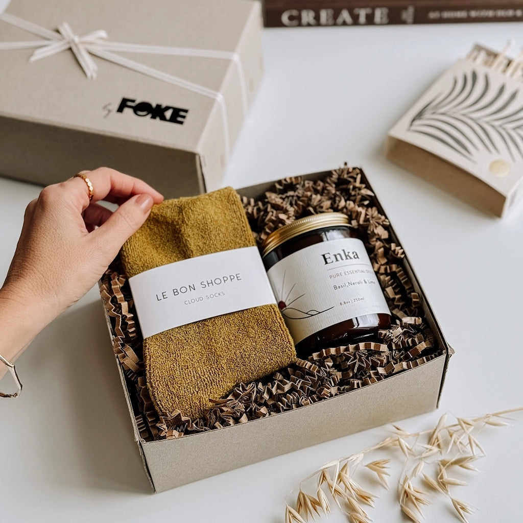 A beautiful photo of byFoke's Chloe Gift Box, opened with the lid to one side. A woman's hand is holding up the corner of the olive Cloud socks which are sitting next to an essential oil candle inside the gift box.