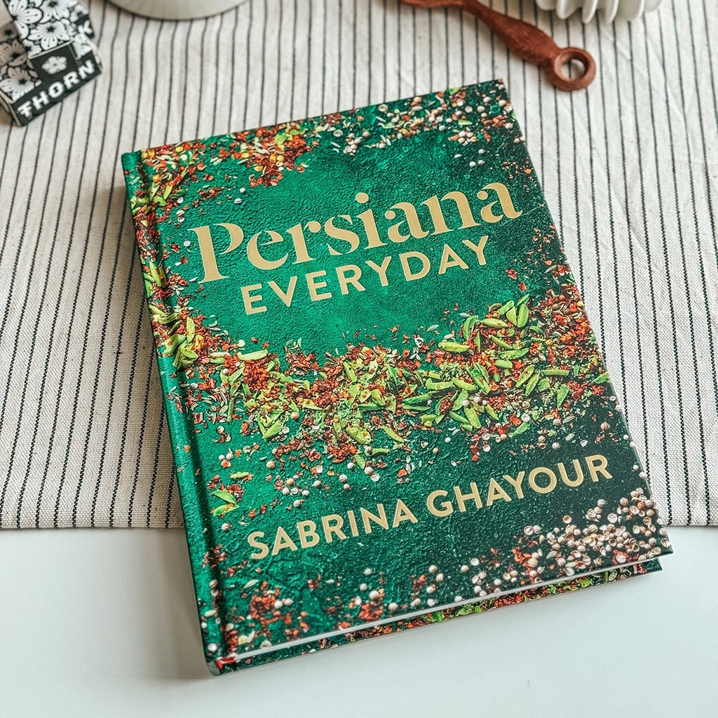 A photograph of book called Persiana Everyday by Sabrina Ghayour lying on a table with a striped tablecloth
