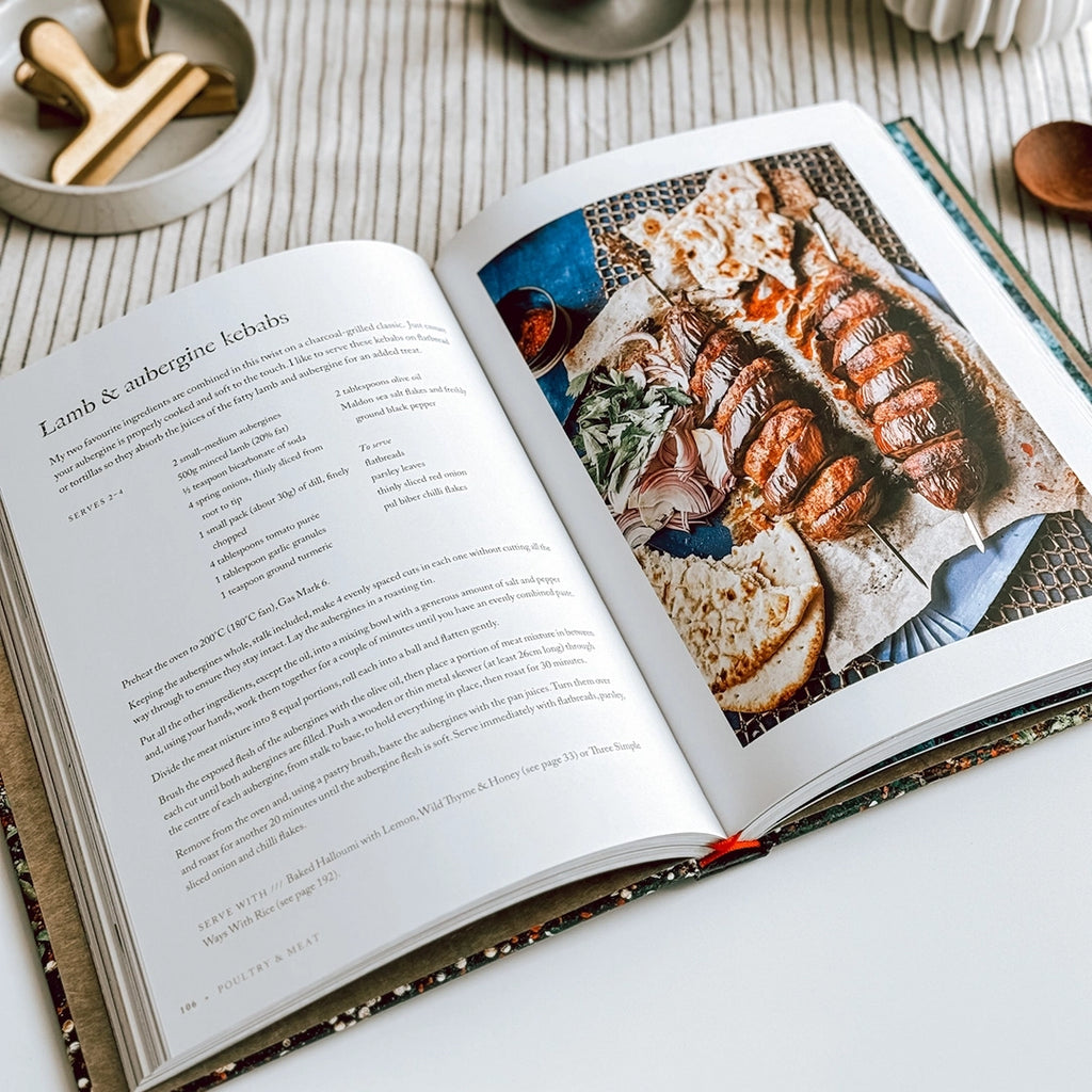 A photograph of the cook book Persiana Everyday by Sabrina Ghayour lying open on a table displaying the recipe for Lamb and aubergine kebabs
