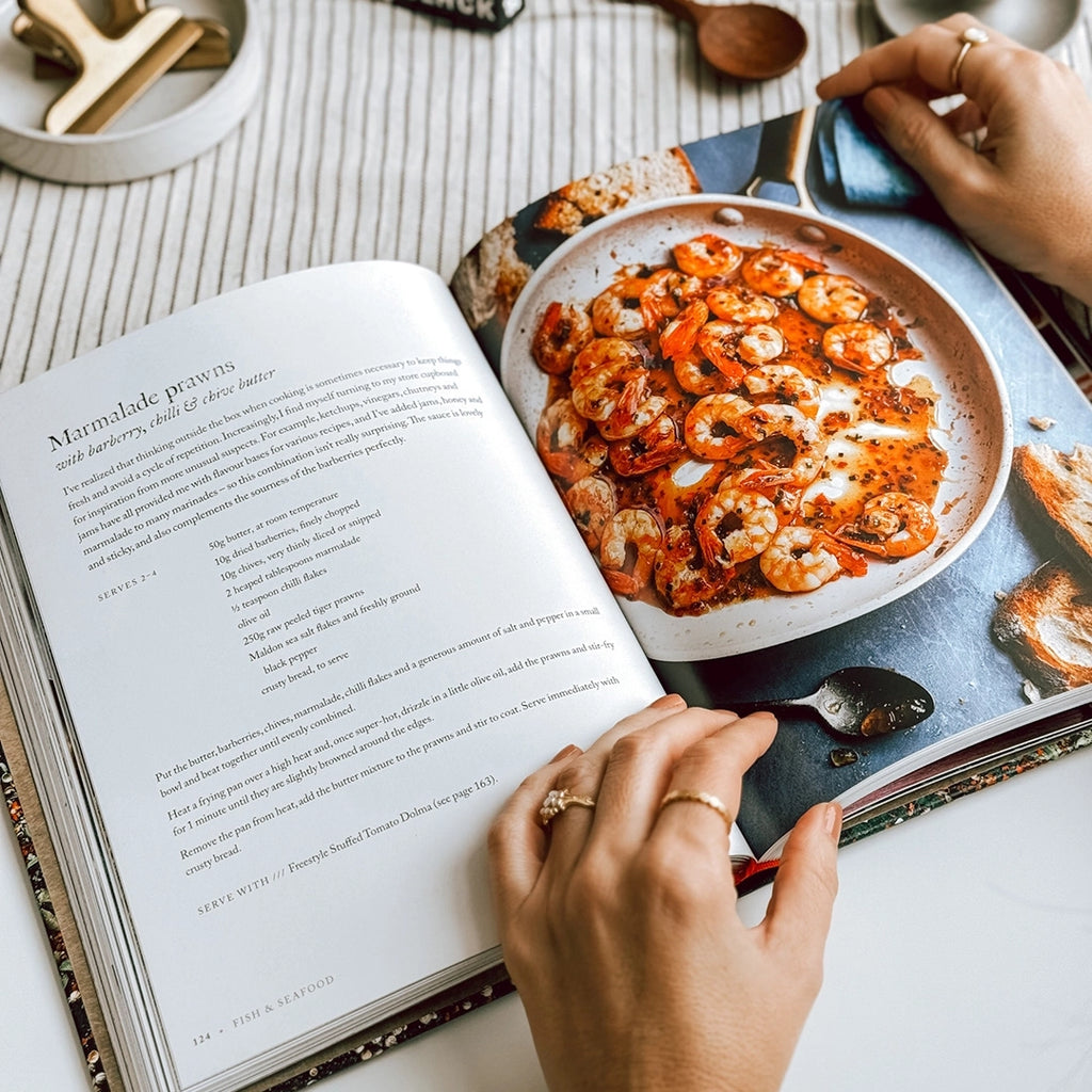 In the photo, "Persiana Everyday" by Sabrina Ghayour is spread open on the table, showcasing the Marmalade prawns recipe