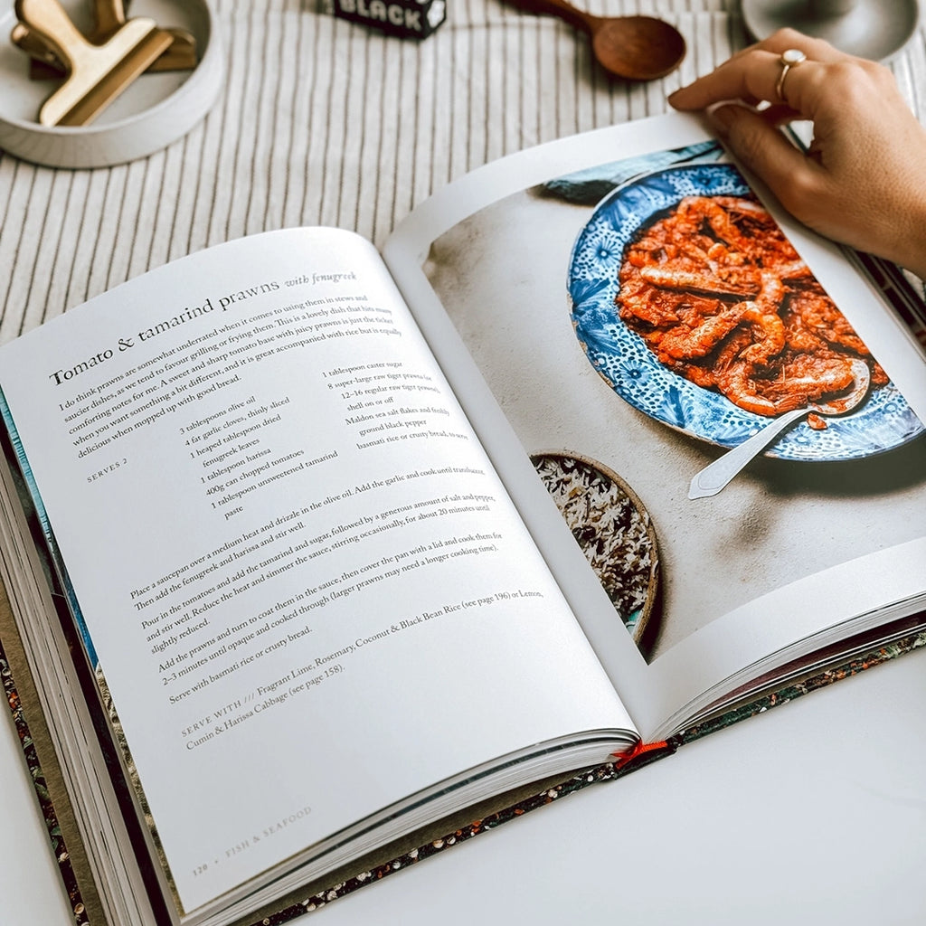On the table, you can see "Persiana Everyday" by Sabrina Ghayour open, highlighting the tomato and tamarind prawns recipe in the photo.