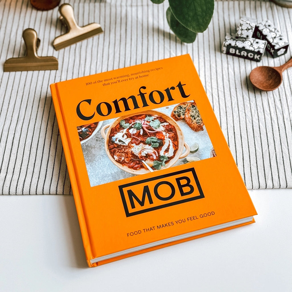 Comfort Mob Cook Book lying closed on a dining table with a striped black and white table cloth.