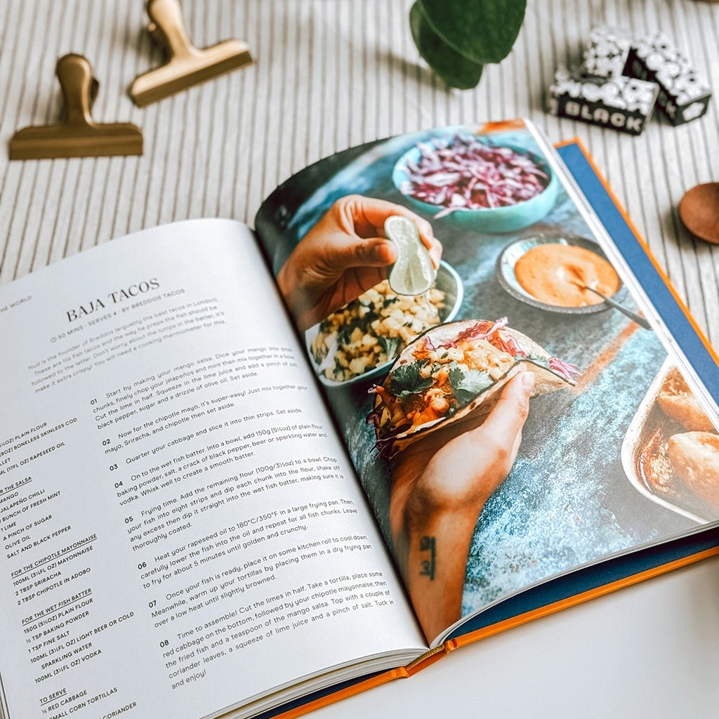 A photo of the Comfort Mob Cook Book is open on the recipe page for Baja Tacos, revealing the tantalising recipe details and a mouthwatering photo of the finished dish.