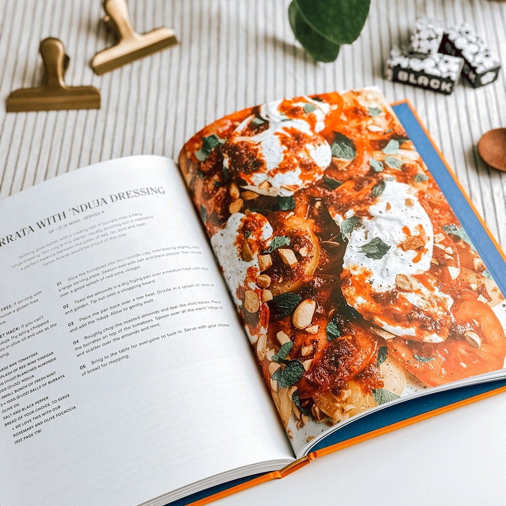 The Comfort Mob Cook Book lying open showing the recipe and photo of Burrata with Nduja Dressing..