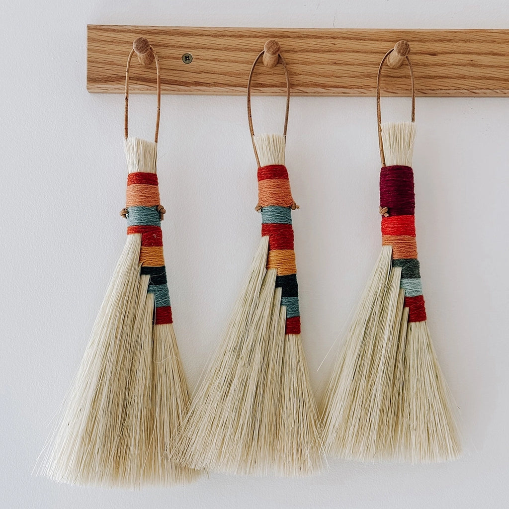 Three handmade Twig Stick Tampico brushes with beautiful coloured woollen handles hanging on an oak peg rack.