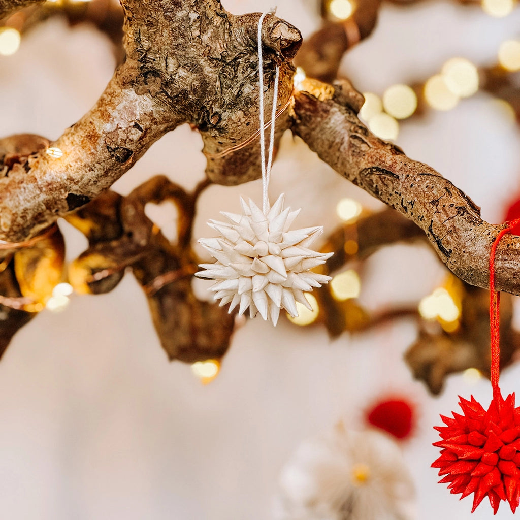 A close up of byFoke's quilled paper Christmas tree decorations in cream and red hanging on a branch with fairy lights.