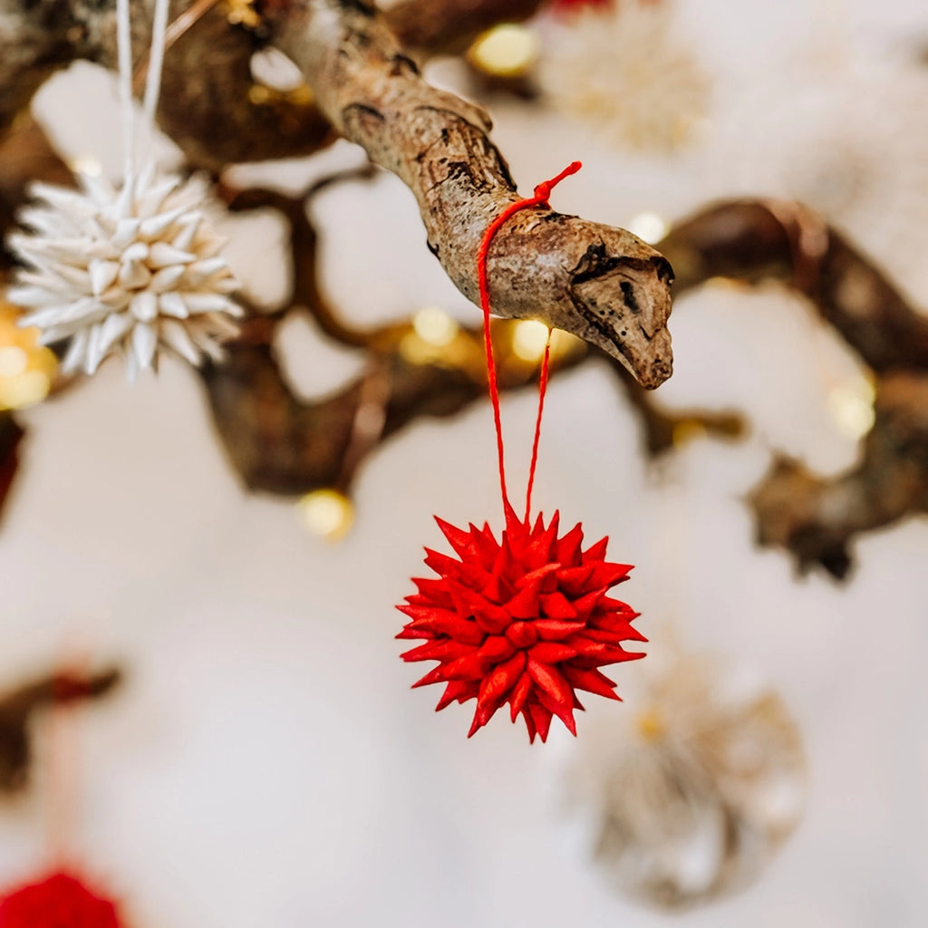 A close up of one of byFoke's quilled paper Christmas tree decorations in red hanging on a branch with fairy lights.