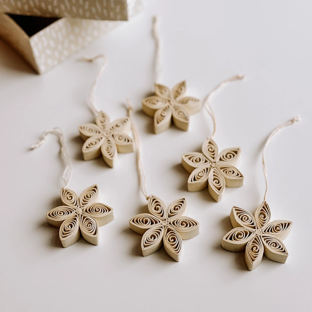 A close up of a set of 6 cream quilled paper star decorations laid out on a table with a beautiful painted paper box in the background.