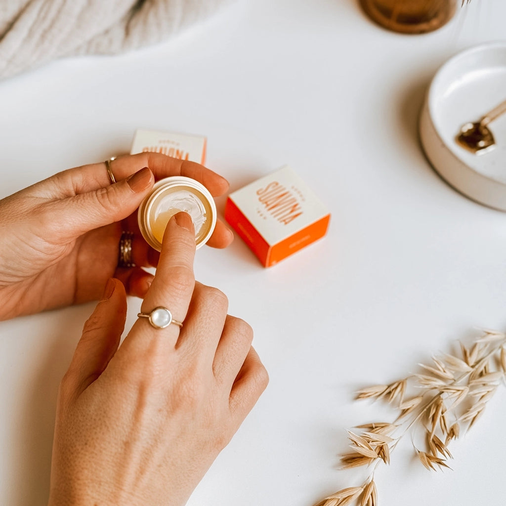 A lady's hands, with her finger inside the pot of Dermo Suavina Lip Balm.