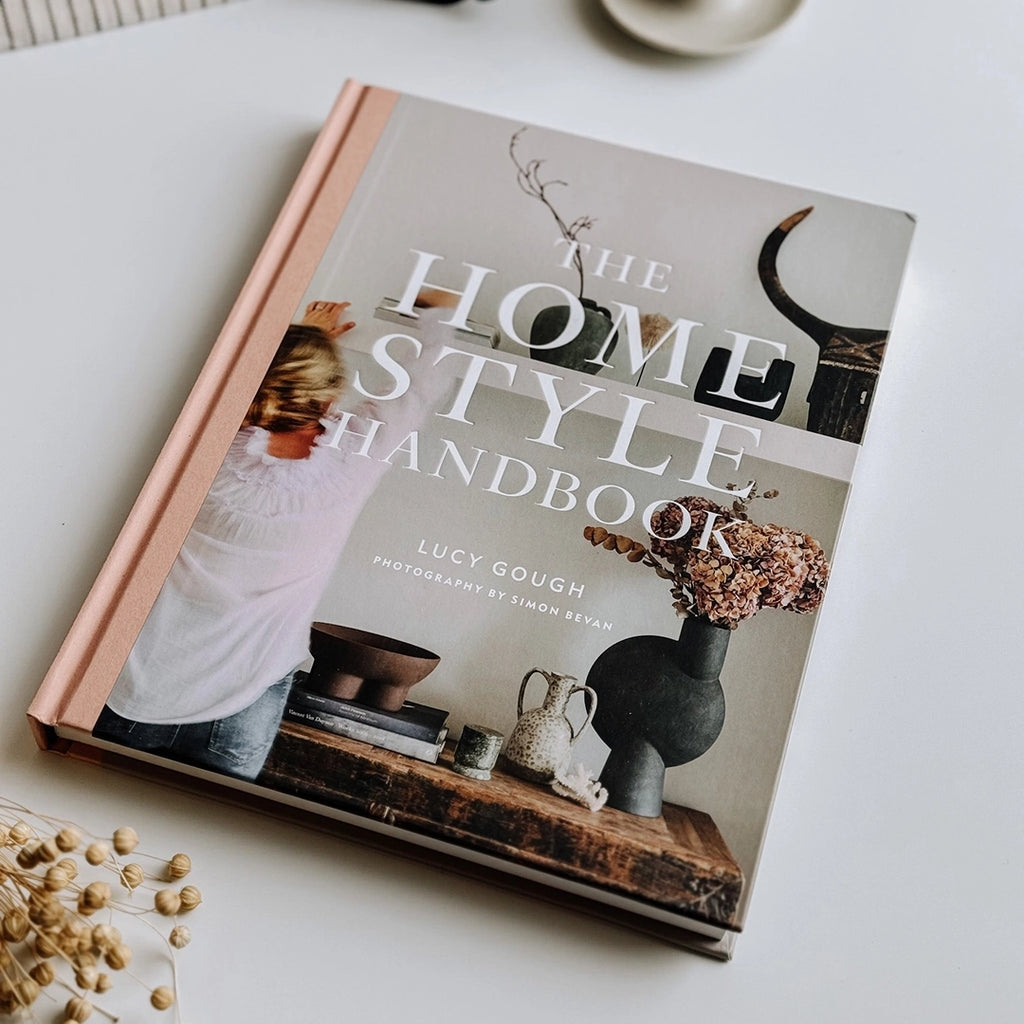 The Home Style Handbook by Lucy Gough, a hard copy version sitting on a table with some dried grasses. byFoke