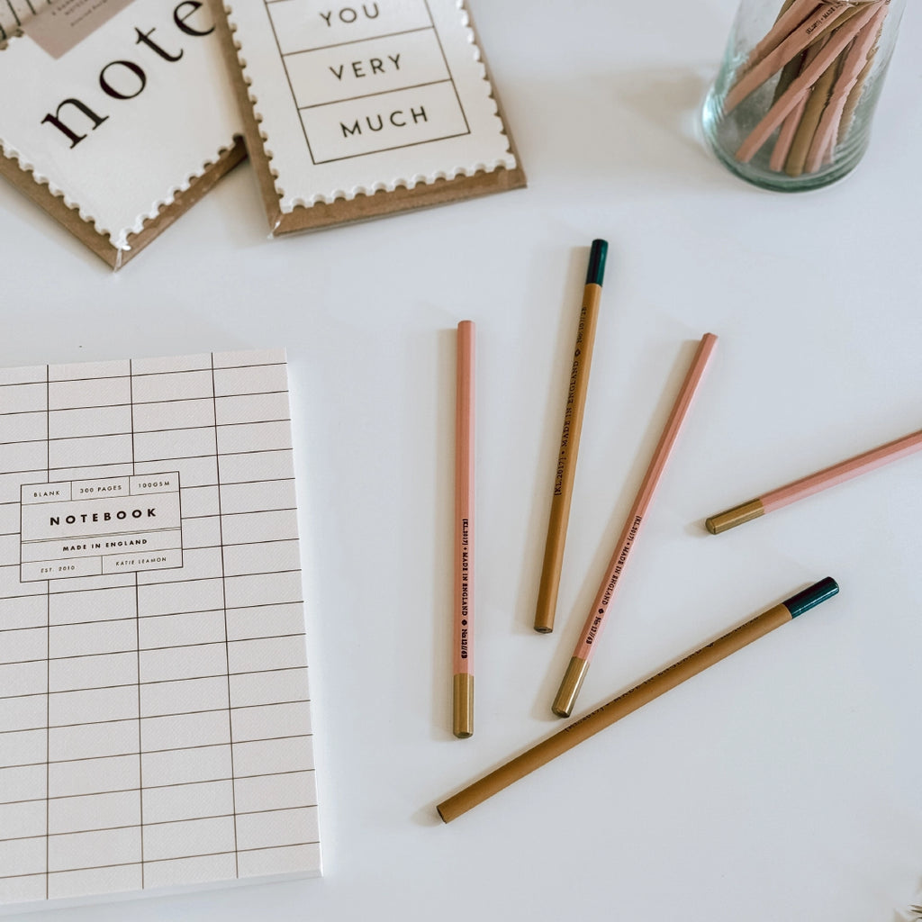 A selection of Katie Leamon pencils, notecards and a notebook laying on a white table at byFoke.