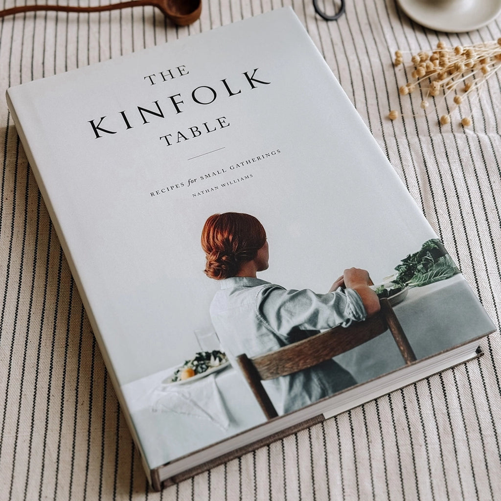 The Kinfolk Table Recipes for Small Gatherings Cook Book. The book is  on a striped table cloth. byFoke