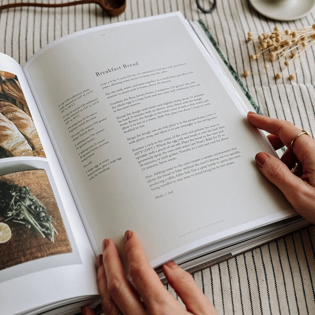A recipe for Breakfast Bread from The Kinfolk Table Recipes for Small Gatherings Cook Book. The book is being held open on the recipe page on a striped table cloth. byFoke