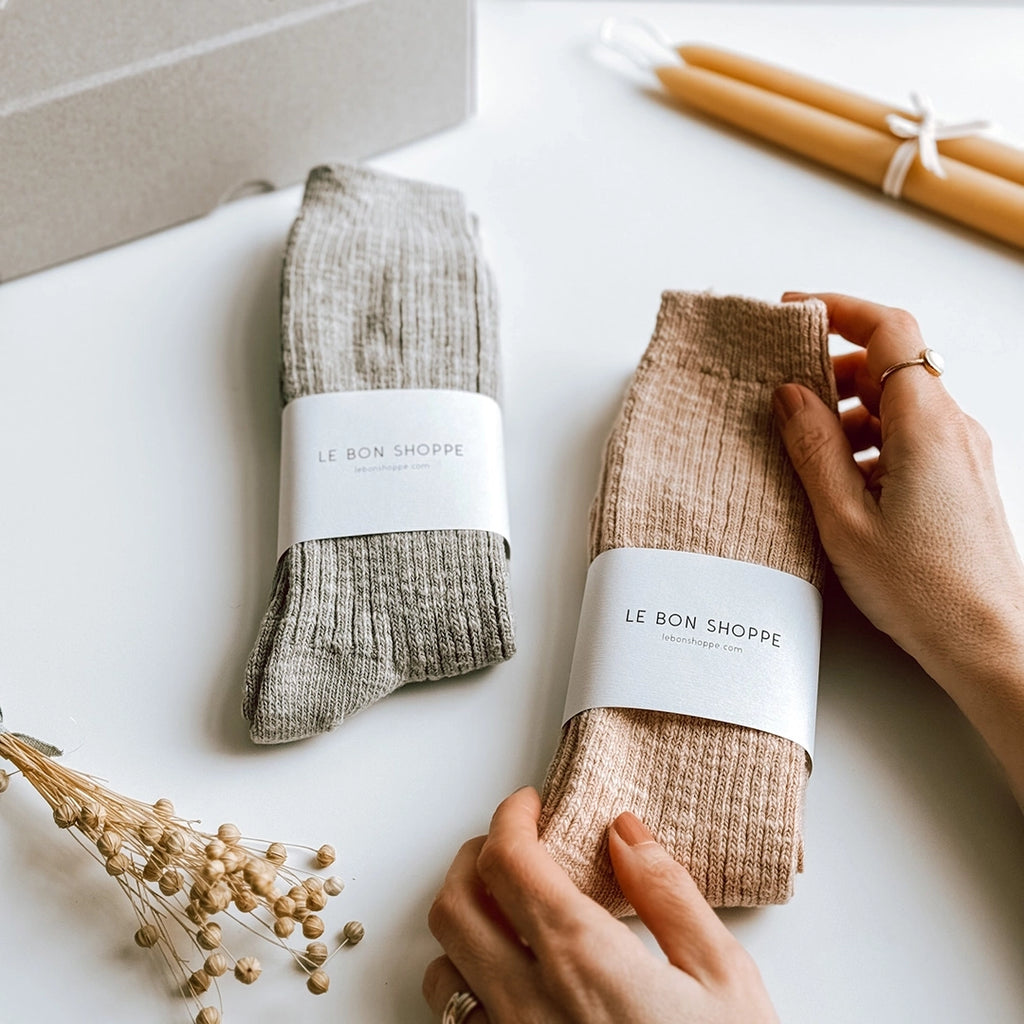 Le Bon Shoppe Cottage Socks in Smoked Sage and Peachy Keen. A woman's hand is holding up one of the pairs of socks. byFoke.