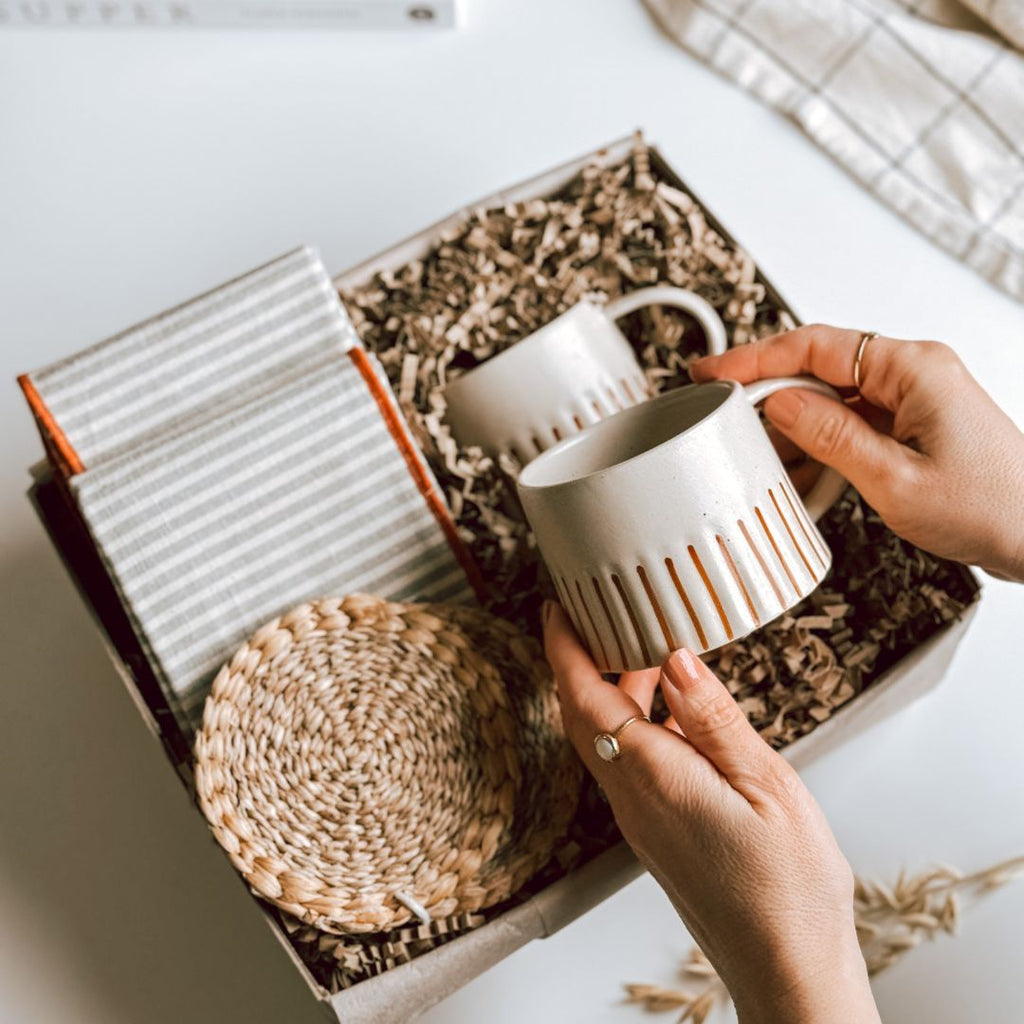 A pair of hands lifting a striped mug out of byFoke's 'Let's Catch Up' Gift Box.