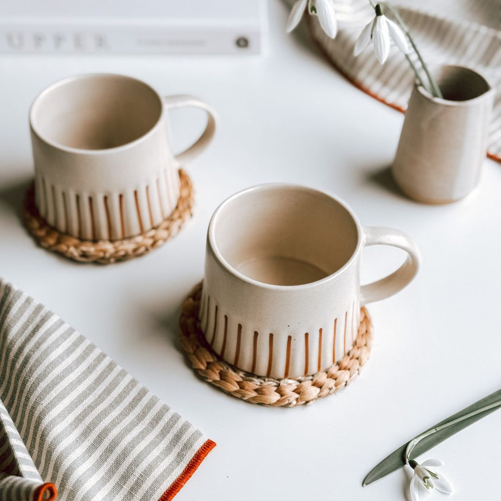 Two Cream and Ginger Striped Mugs on woven coasters with striped napkins.