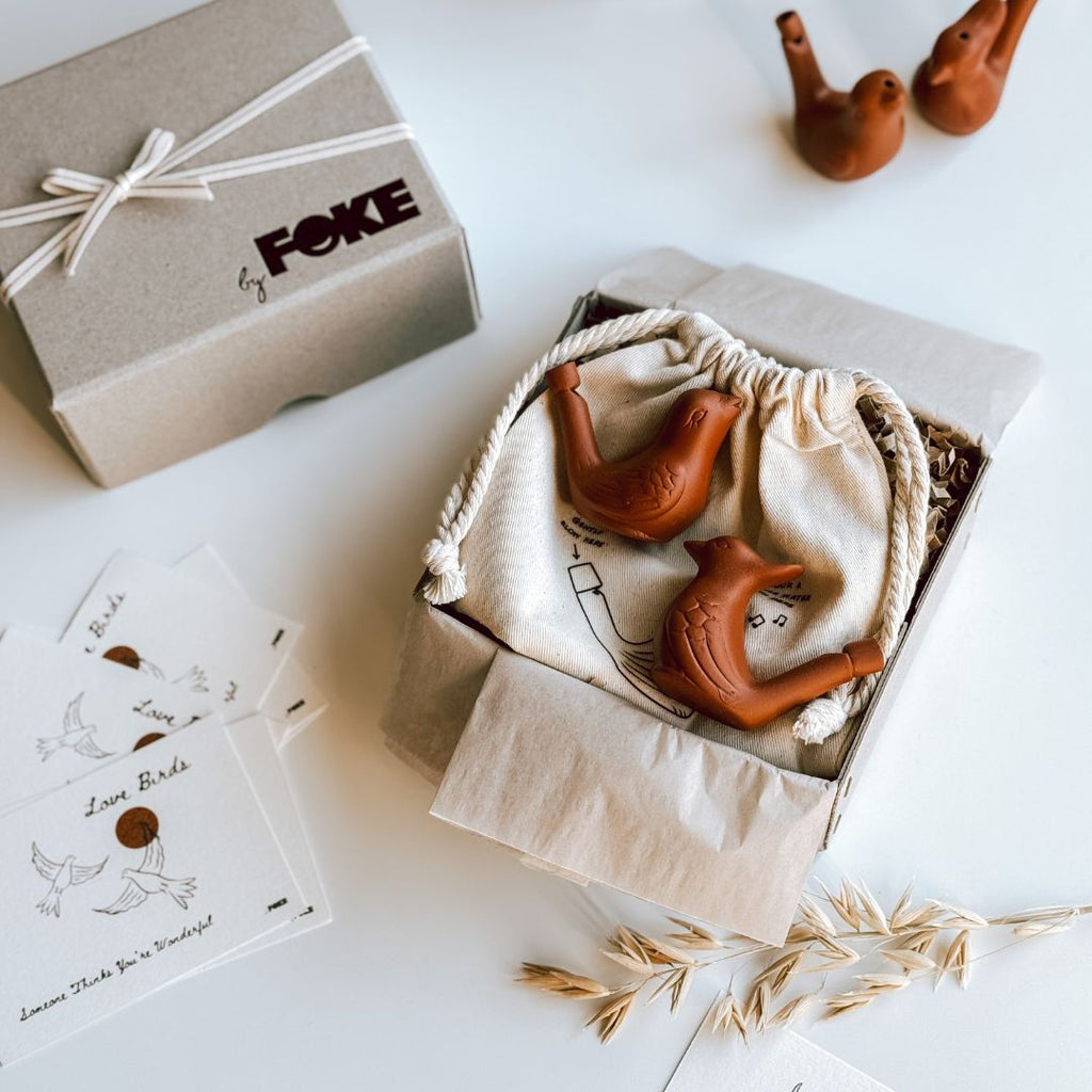 An open byFoke Gift Box containing 2 ceramic bird whistles on a cotton pouch.