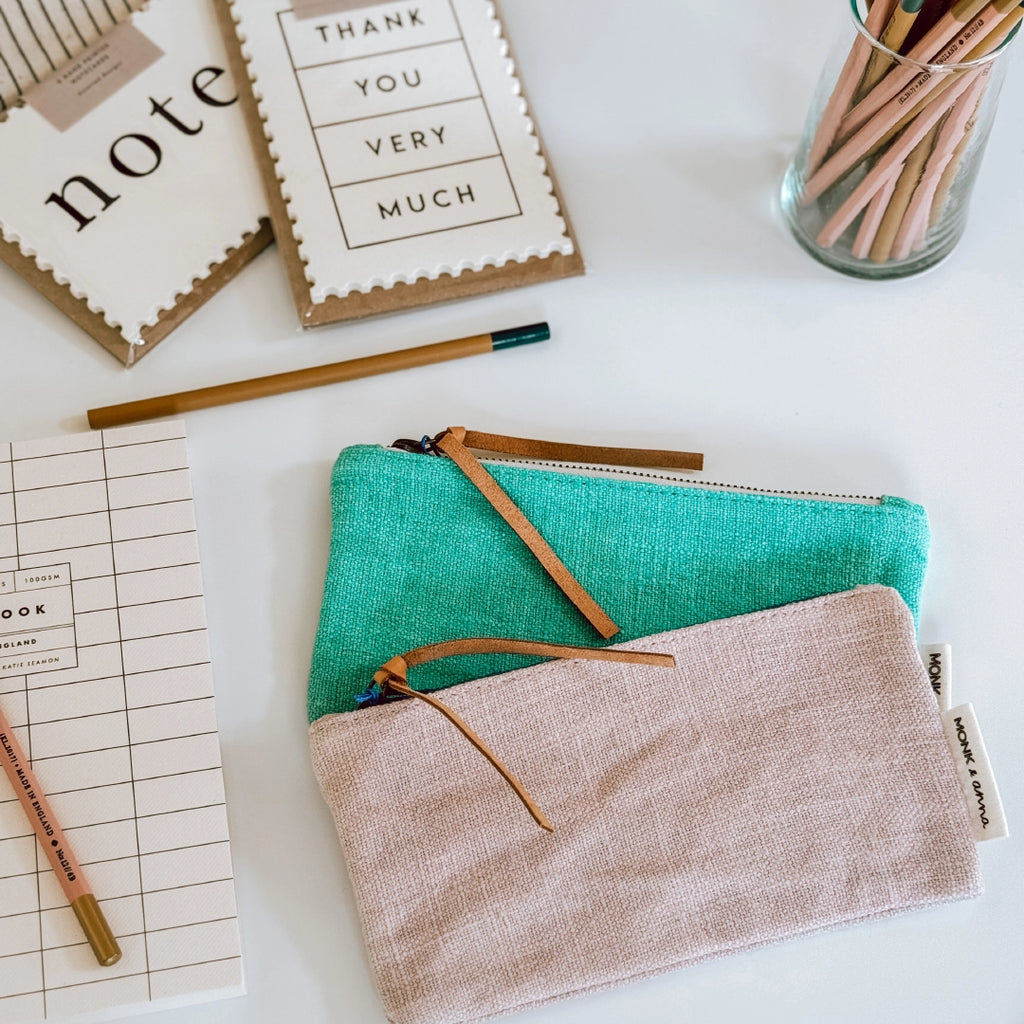 Two Monk & Anna linen pencil cases, one pink, one green, on a table in the byFoke studio with pencils and notecards in the background.