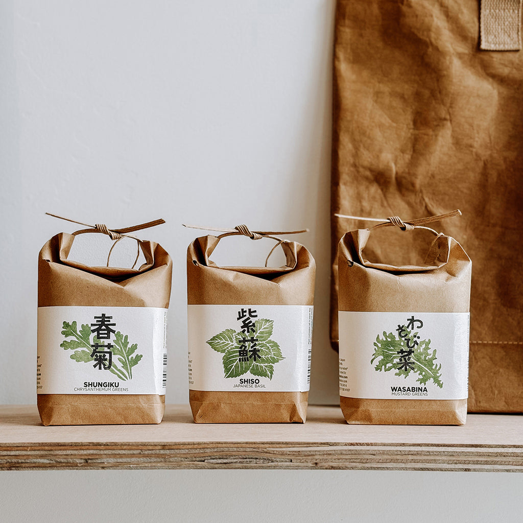 Three Cultivate & Eat, Japanese Herb Kits lined up on a plywood shelf in their Kraft paper bag packaging. On display in the byFoke gift shop.