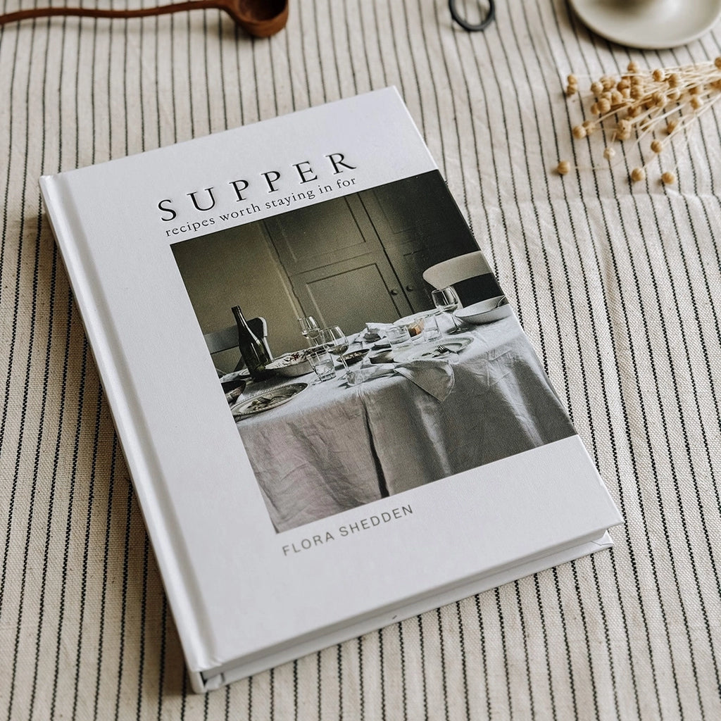 Supper, recipes worth staying in for by Flora Shedden. A copy of the cook book is laying on table with a striped table cloth. byFoke