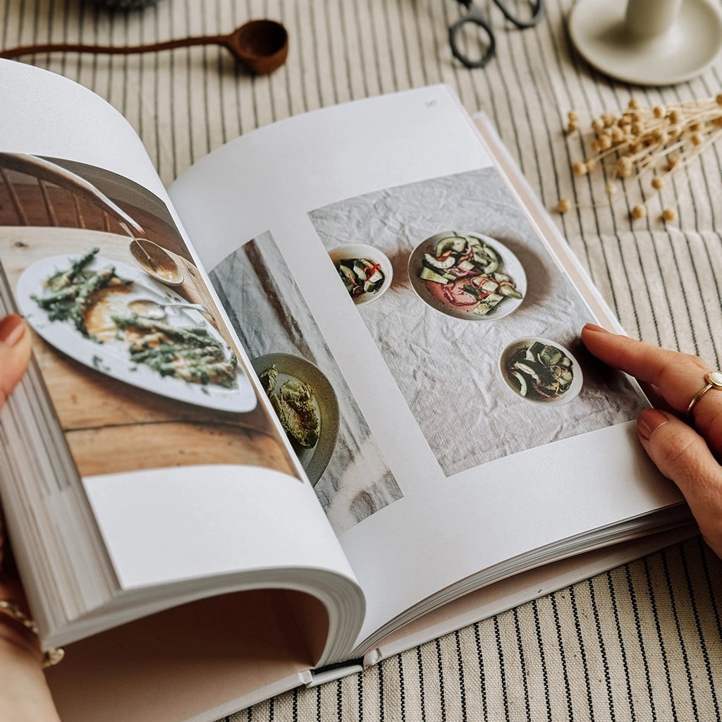 Supper, recipes worth staying in for by Flora Shedden. The cook book is being held open, showing the photography inside. The book is on table with a striped table cloth. byFoke
