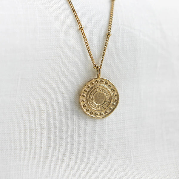A close up of the Alba Necklace by Agape Studio. The necklace is a round gold pendant on a fine gold chain.