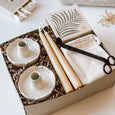 An open byFoke Cora gift box containing a set of two stoneware flower candle holders, a pair of beeswax taper candles, luxury letterpress matches by Archivist and a pair of candle wick trimmers.