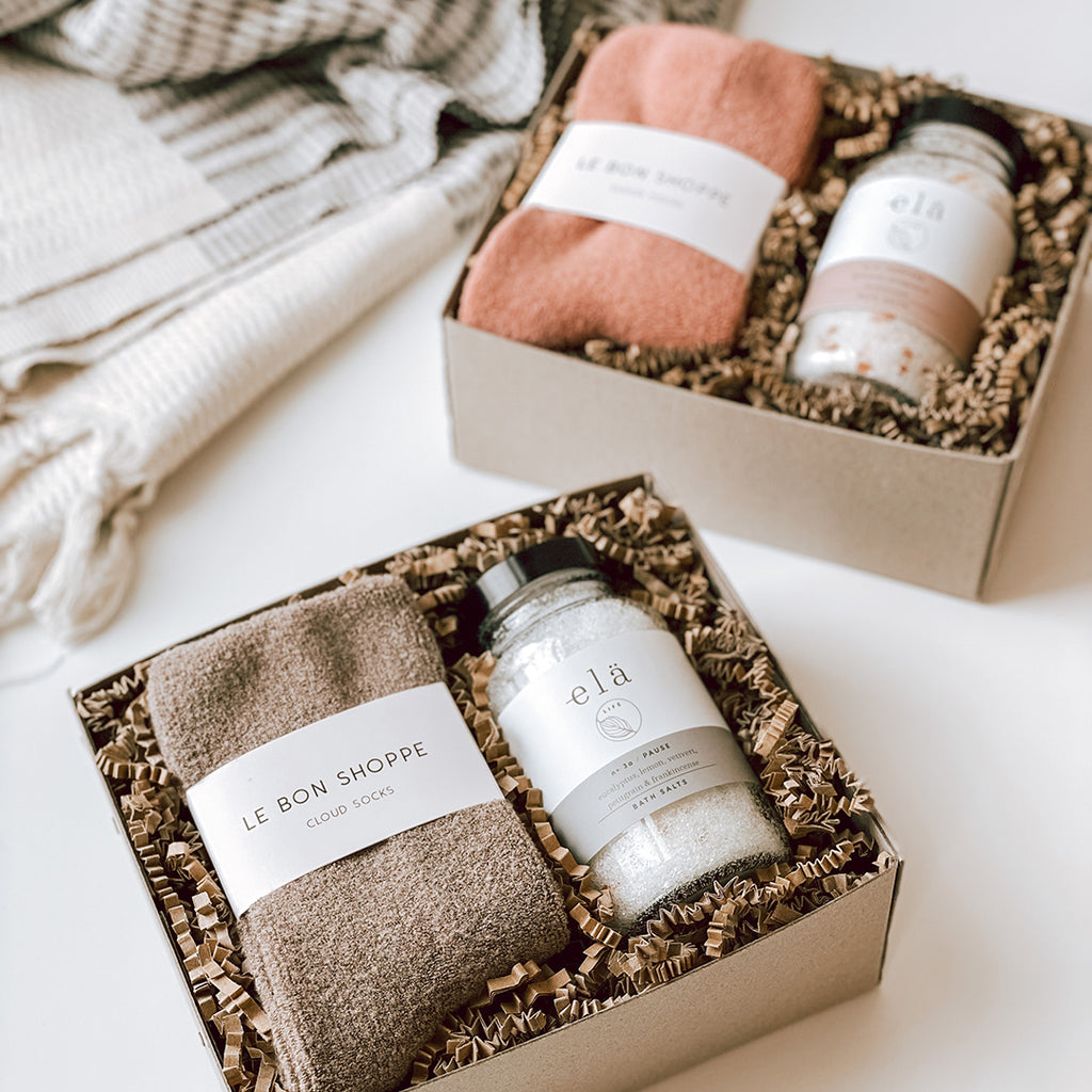 Two byFoke Erin Gift Boxes, one in the Mulberry colour way and the other in the Frappe colour way. Both boxes are open and contain cloud socks by Le Bon Shoppe and Ela Life Bath Salts.