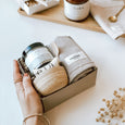 A woman's hand holding a byFoke Eve gift box containing the Ela Life Kaolin Clay Face Mask Set and Calm wash cloth by The Organic Company. 