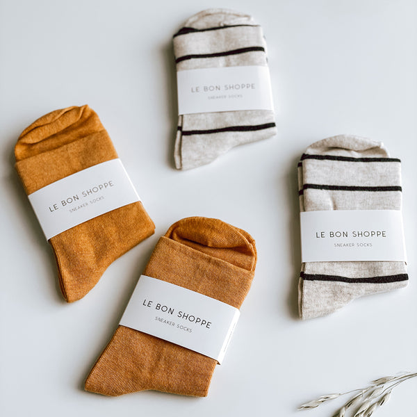 Sneaker Socks in Marigold and Wally Socks in Grain with a black stripe. The socks are all made by Le Bon Shoppe and are photographed on a white background.