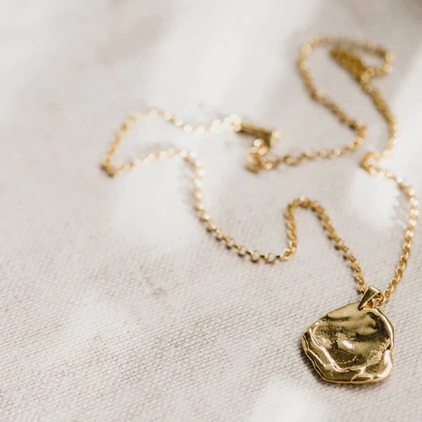 A close up of Matthew Calvin's Antigua Gold Necklace lying on a piece of cream textured linen.