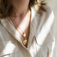 A women's neck wearing two gold necklaces and a cream cotton shirt. Both necklaces are made by Matthew Calvin one is the Oro necklace in gold and the other is the Antigua necklace in gold.