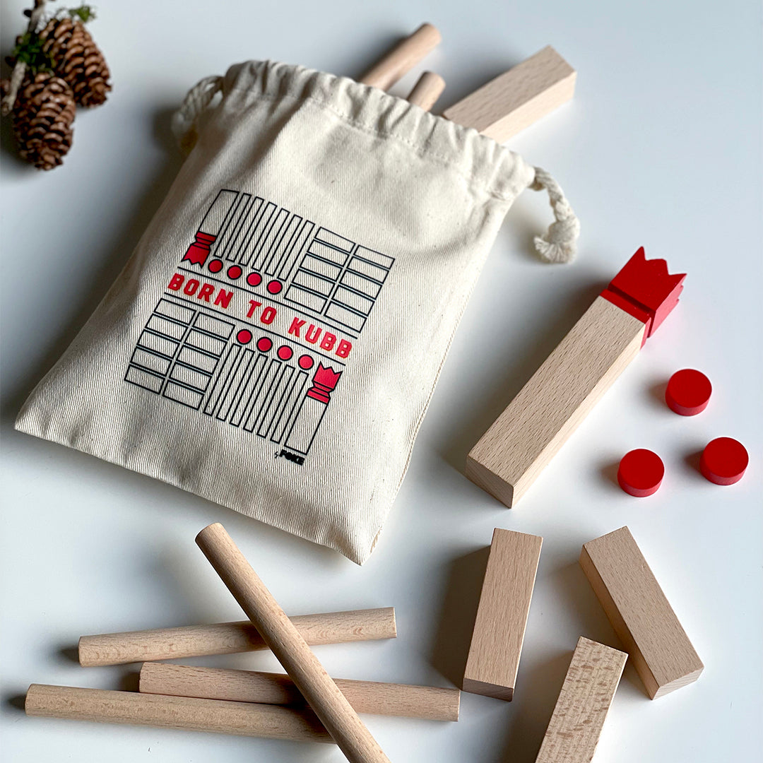 byFoke mini Kubb game in a cotton pouch. The wooden Kubb game is laid out on a table beside the pouch that the game comes in.